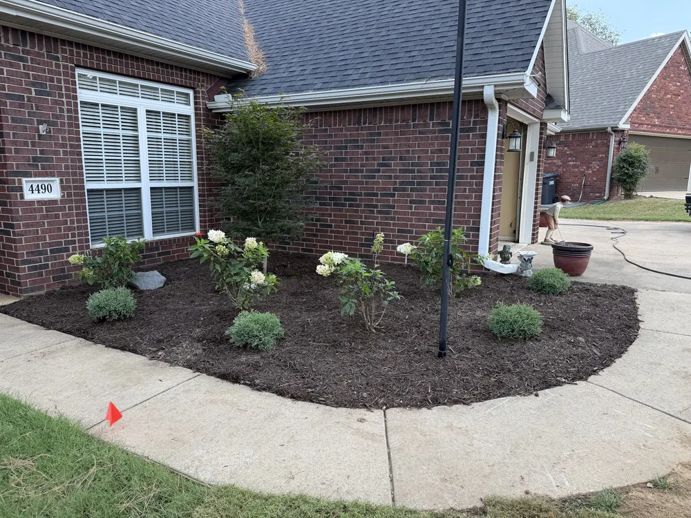 Curved concrete walk running past a planted mulch bed along the front of a brick house