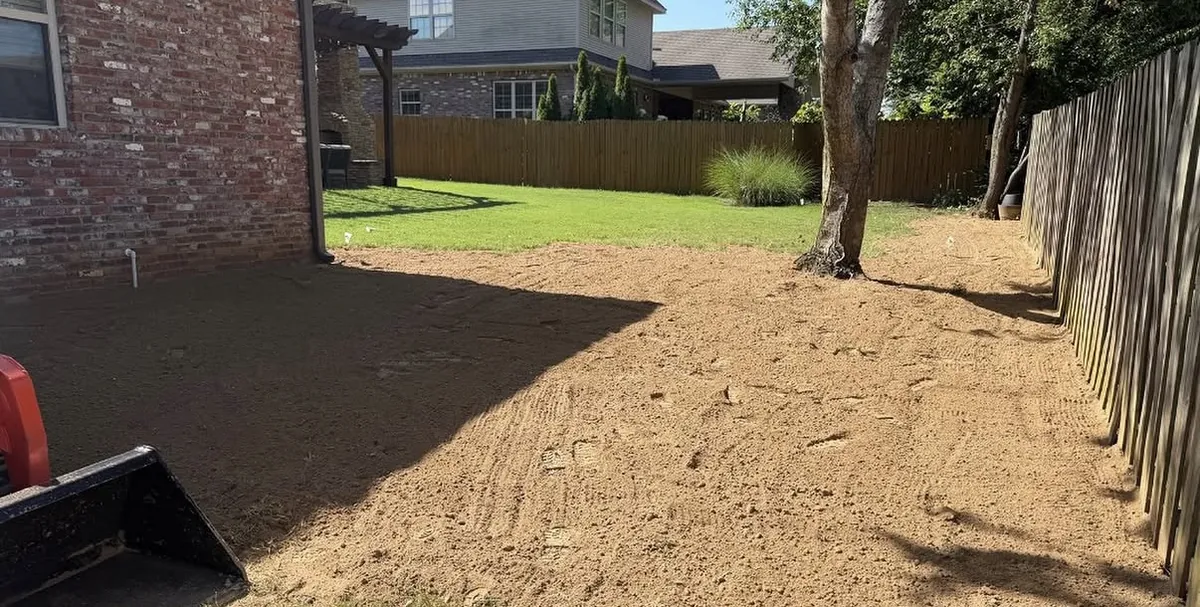 Back yard stripped to bare graded dirt before the sod went down, with the fence and tree in place