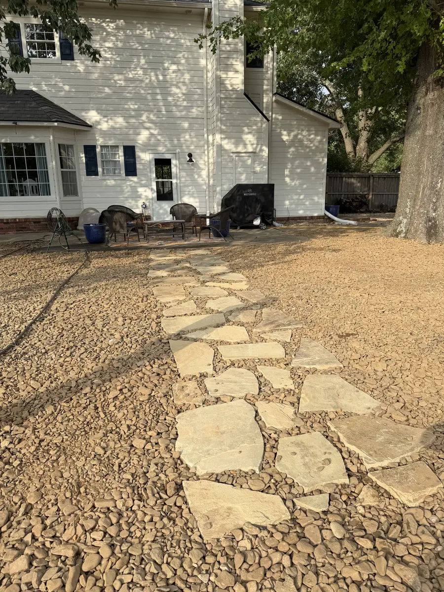 The finished flagstone stepping stone path set into river rock, running from the patio out across the same yard