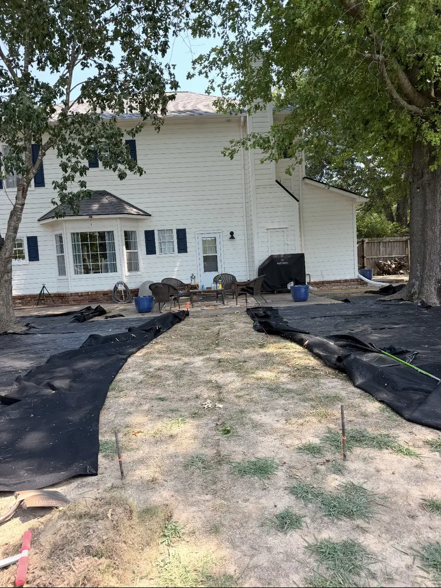 The back yard before the path went in: landscape fabric pinned out over bare ground with marker stakes set along the line of the walkway