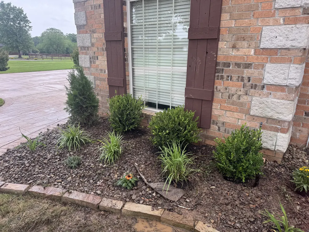 Planting bed of shrubs and grasses in a brick edged rock bed along the corner of a brick house