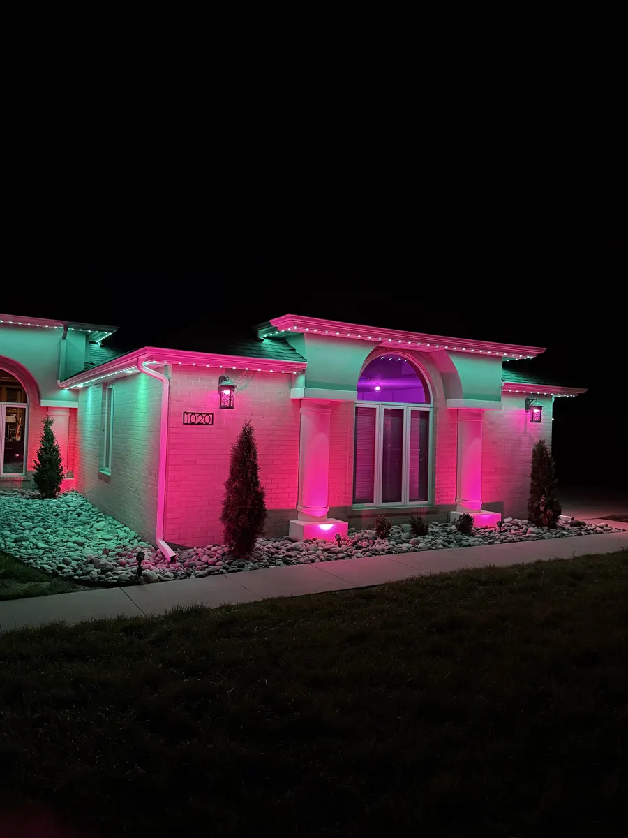 Stucco home at night with the roofline and columns lit in pink and teal