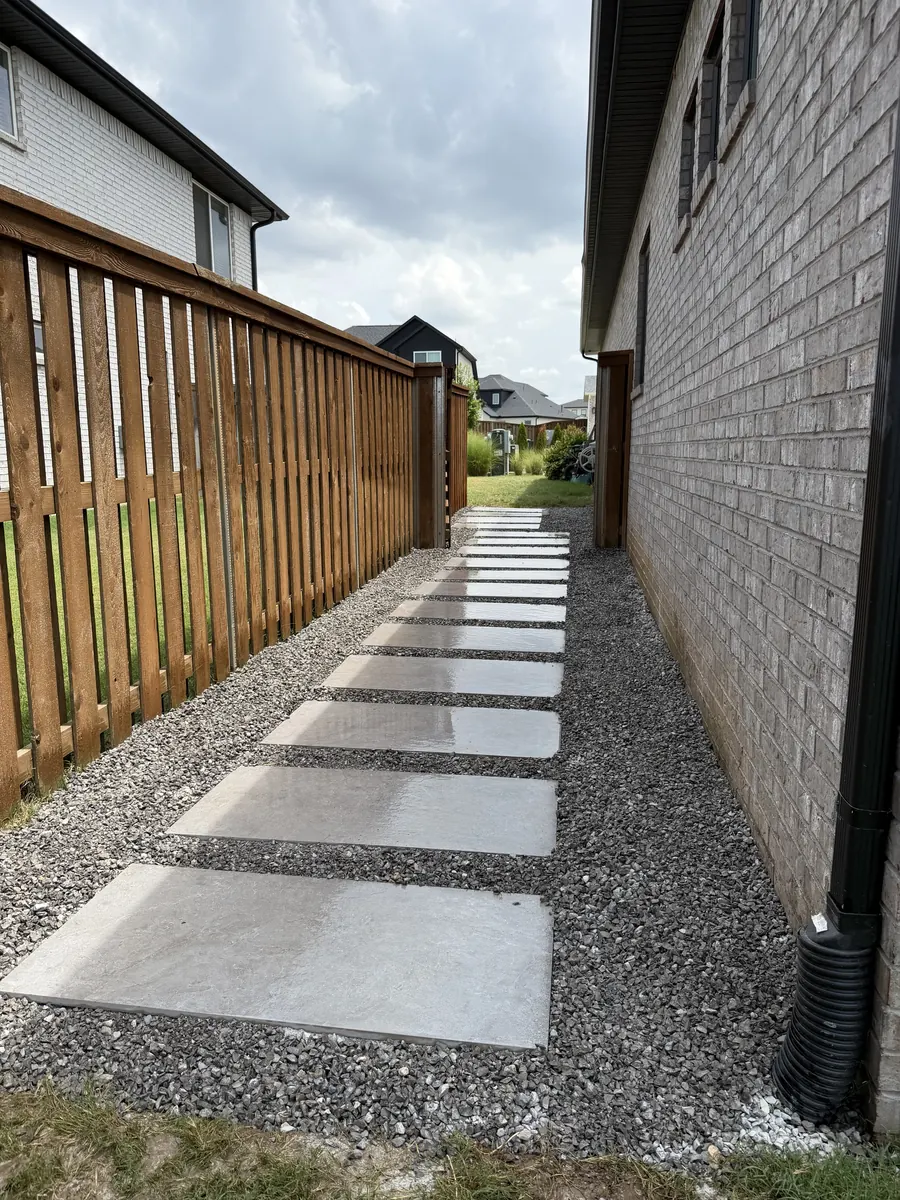 Concrete slab stepping path set in grey gravel between a wood fence and a brick wall