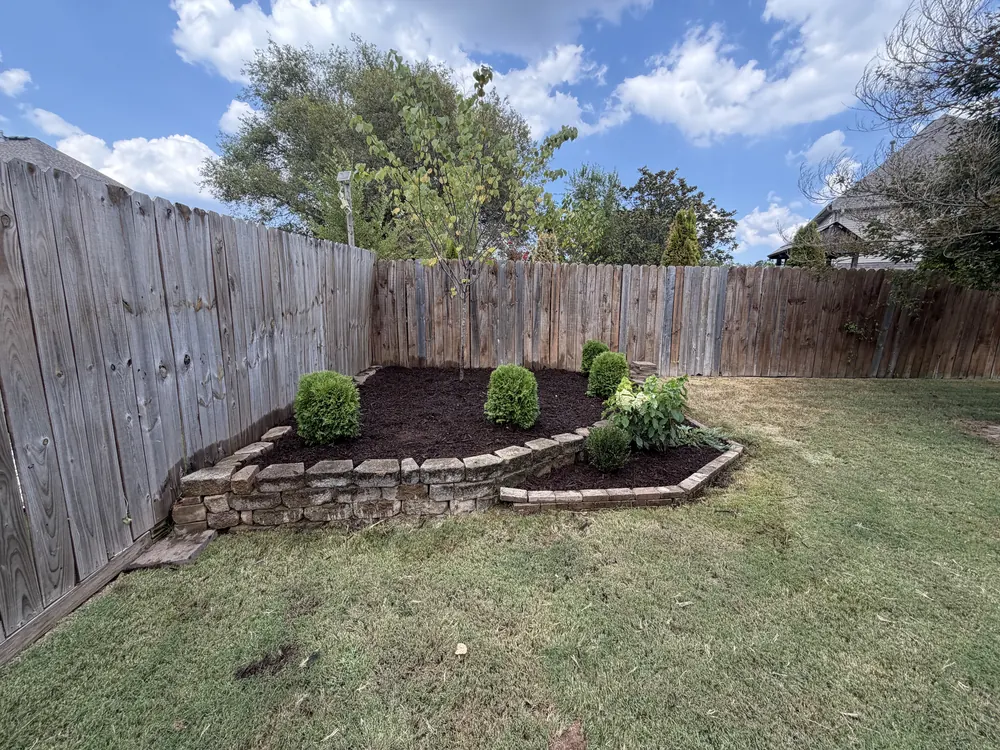 Stacked stone border wall holding a planted bed along a wood fence