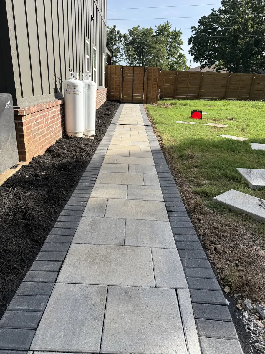 Paver walkway with a charcoal border running the length of the house between the wall and the fence
