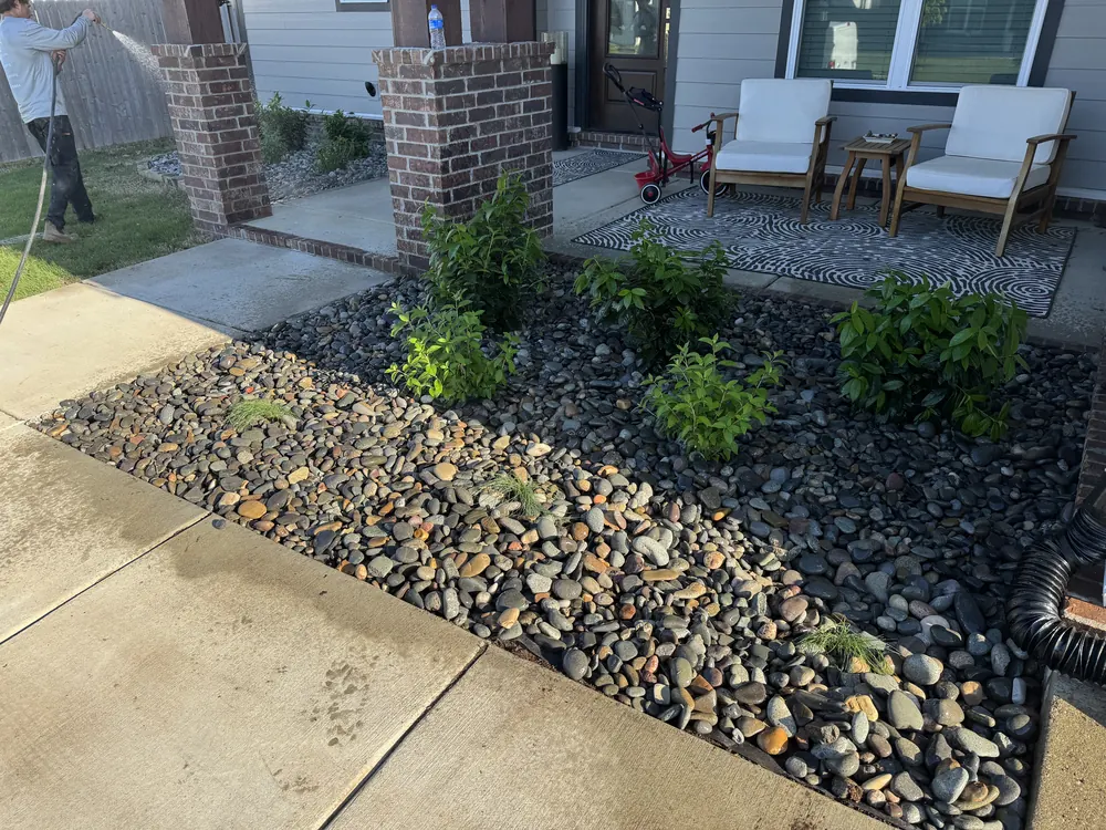 River rock bed planted with shrubs running along a concrete walk beside a patio