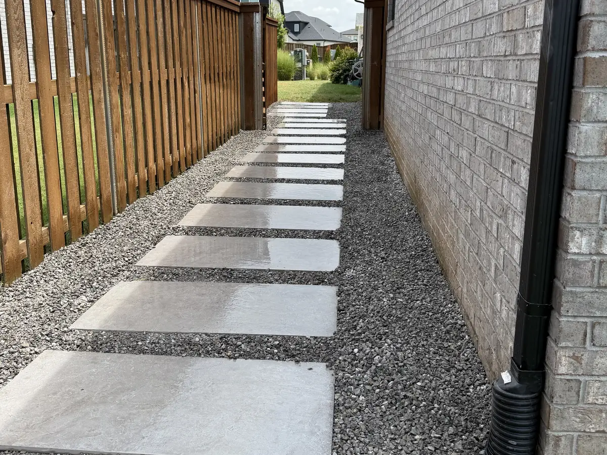 Large concrete slabs laid as a stepping path in grey gravel down the side of a brick house